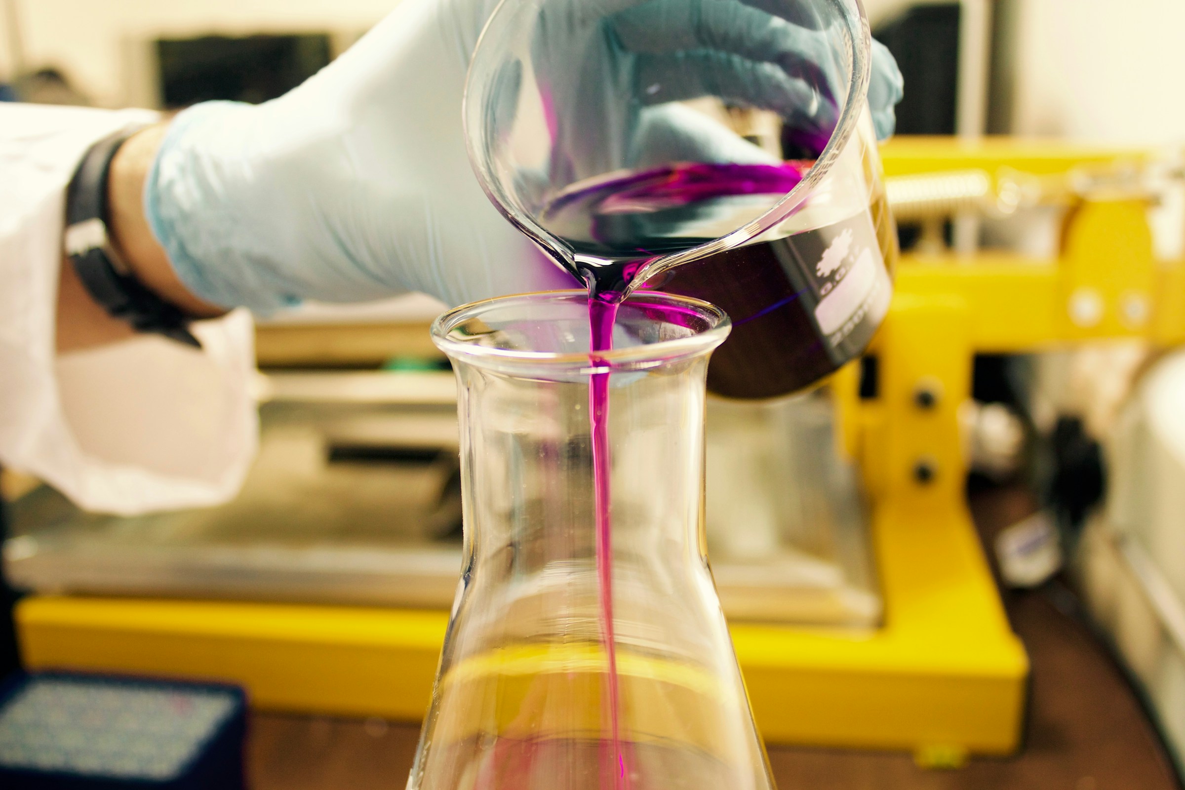 Transparent laboratory vessel with liquid being poured under soft light